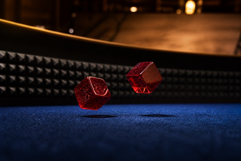 Zwei rote Würfel im Flug dicht über dem lapisblauen Filz eines Craps-Tisches, dahinter die genoppte Bande